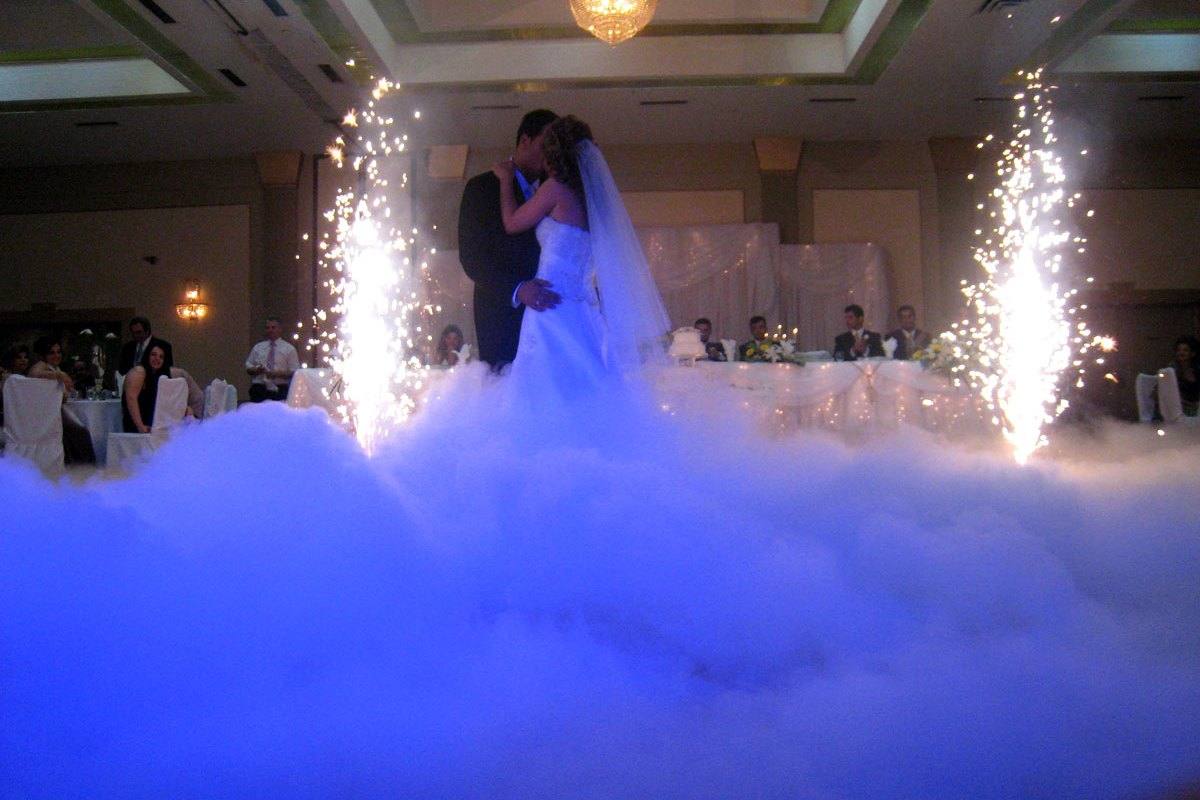Newlyweds sharing their first dance above a low cloud, framed by warm spark fountains