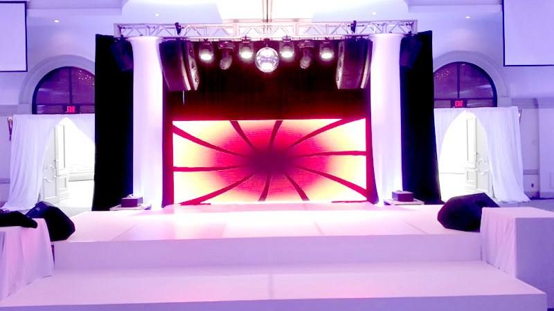 Stage deck built with a lit screen behind it and truss either side