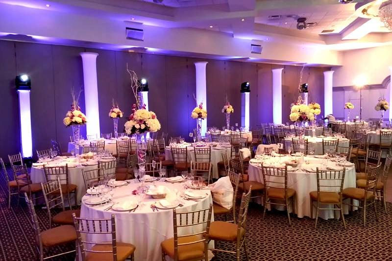 Banquet room uplit violet with tall floral centrepieces on set tables