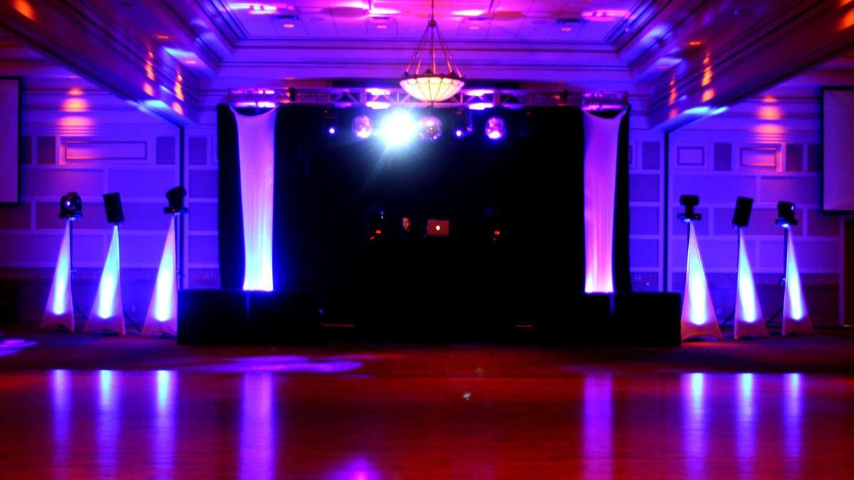 Banquet hall under magenta and violet uplighting, chandelier lit, tables set