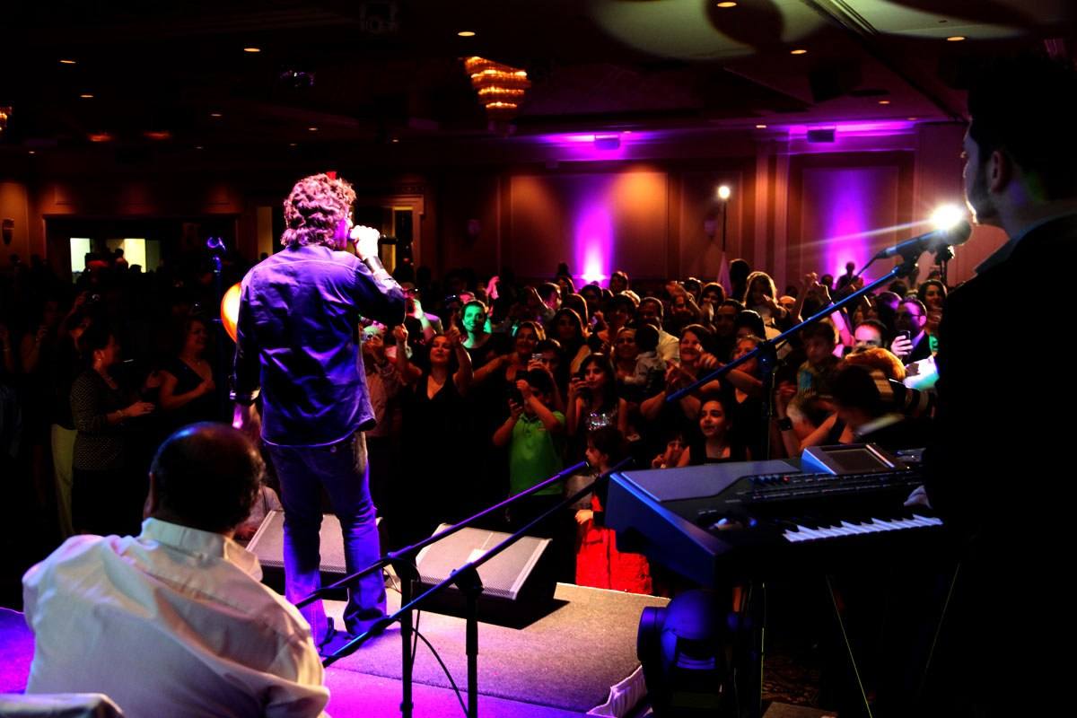 Band playing to a standing crowd, vocalist front of stage under warm light